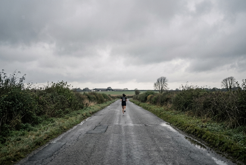 A lone runner on a long weekend run along an open country road